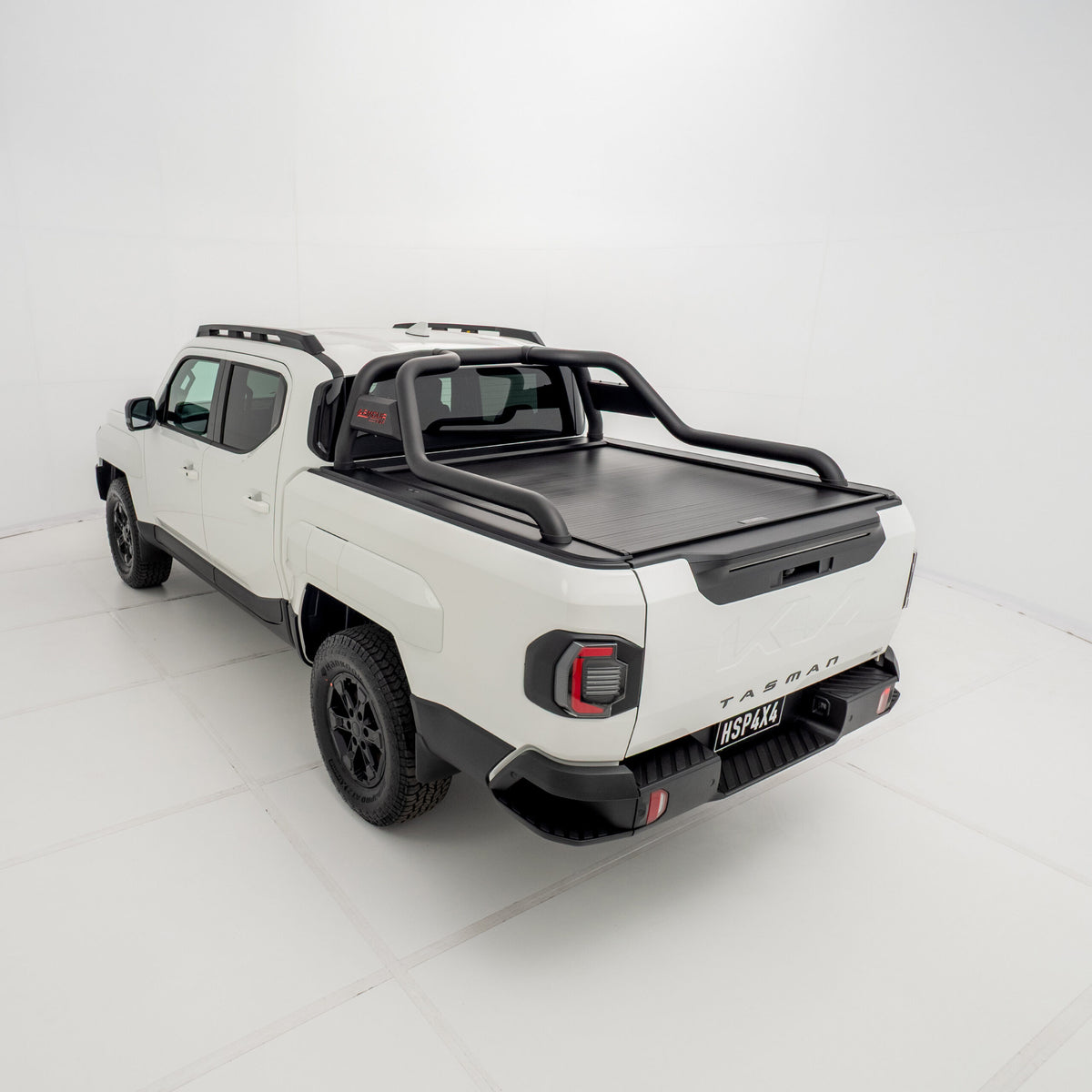 Angled 3/4 rear view of a white Kia Tasman fitted with an HSP Roll R electric roller cover in the closed position with black sports bars mounted.
